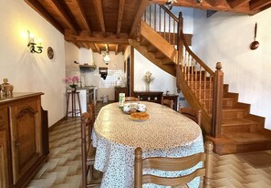 Una cucina con un tavolo rotondo, sedie di legno, una scala e un soffitto in legno.