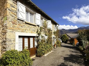 Ein Steinhaus mit einer Holztür, einem Fenster mit Vorhang und Blick auf Berge im Hintergrund.