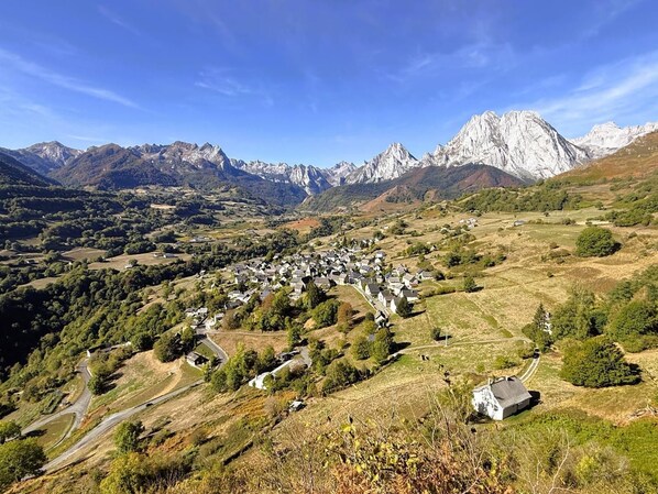 Un paesaggio montuoso con un villaggio situato tra dolci colline e imponenti cime sullo sfondo.