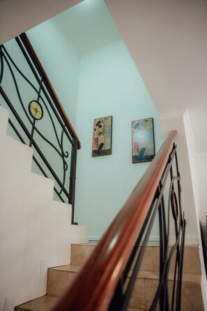 Eine Holzhandläufung und schwarze Metallspindeln säumen eine Treppe, die zu einer Zwischenebene mit zwei gerahmten Kunstwerken führt.