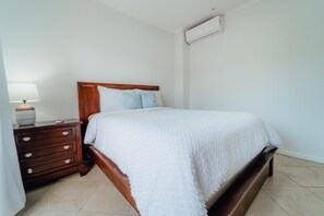 A bedroom with a wooden bed, a nightstand with a lamp, and a wall-mounted air conditioner. - 4BR Townhome-Private Hot Tub & Gazebo w/ Pool, Gym (Noord)