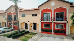 A residential building with a red and beige facade, multiple balconies, and a well-maintained front yard. - 4BR Townhome-Private Hot Tub & Gazebo w/ Pool, Gym (Noord)