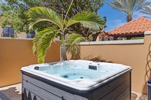 Ein Whirlpool in einer Außenanlage mit einer Palme und einem Ziegeldach im Hintergrund.