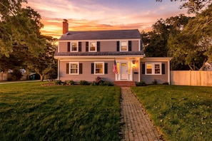 A two-story house with a front porch, a brick pathway leading to the entrance, and an American flag. - Paws on Murphy - Near Beaches & Main Street (Hyannis)