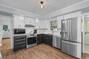 A modern kitchen with white cabinets, stainless steel appliances, and a wooden floor. - Paws on Murphy - Near Beaches & Main Street (Hyannis)