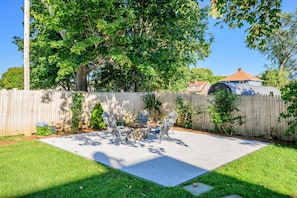 A backyard with a patio table and chairs, surrounded by a wooden fence and trees. - Paws on Murphy - Near Beaches & Main Street (Hyannis)