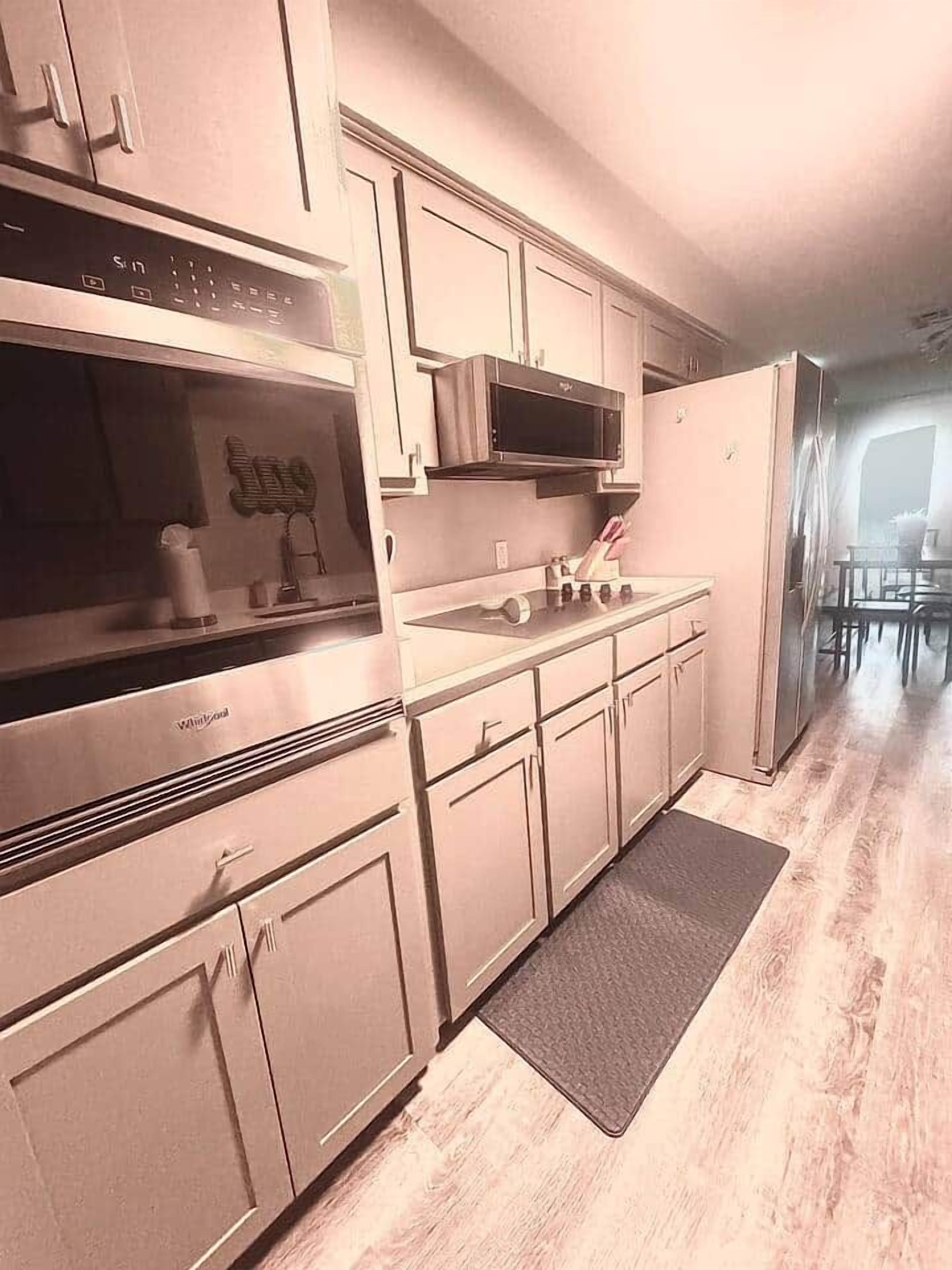 A kitchen with stainless steel appliances, white cabinets, and a wooden floor.