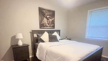 Een slaapkamer met een bed, nachtkastje, lamp, plafondventilator en een raam met jaloezieën.
