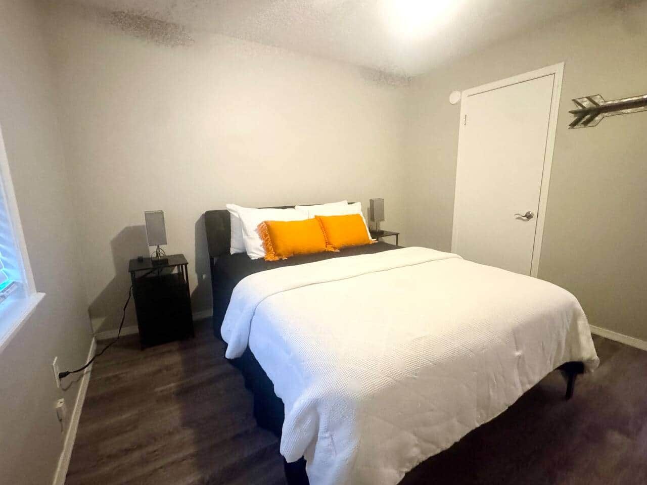 Un dormitorio con cama, mesitas de noche, una puerta y una ventana.