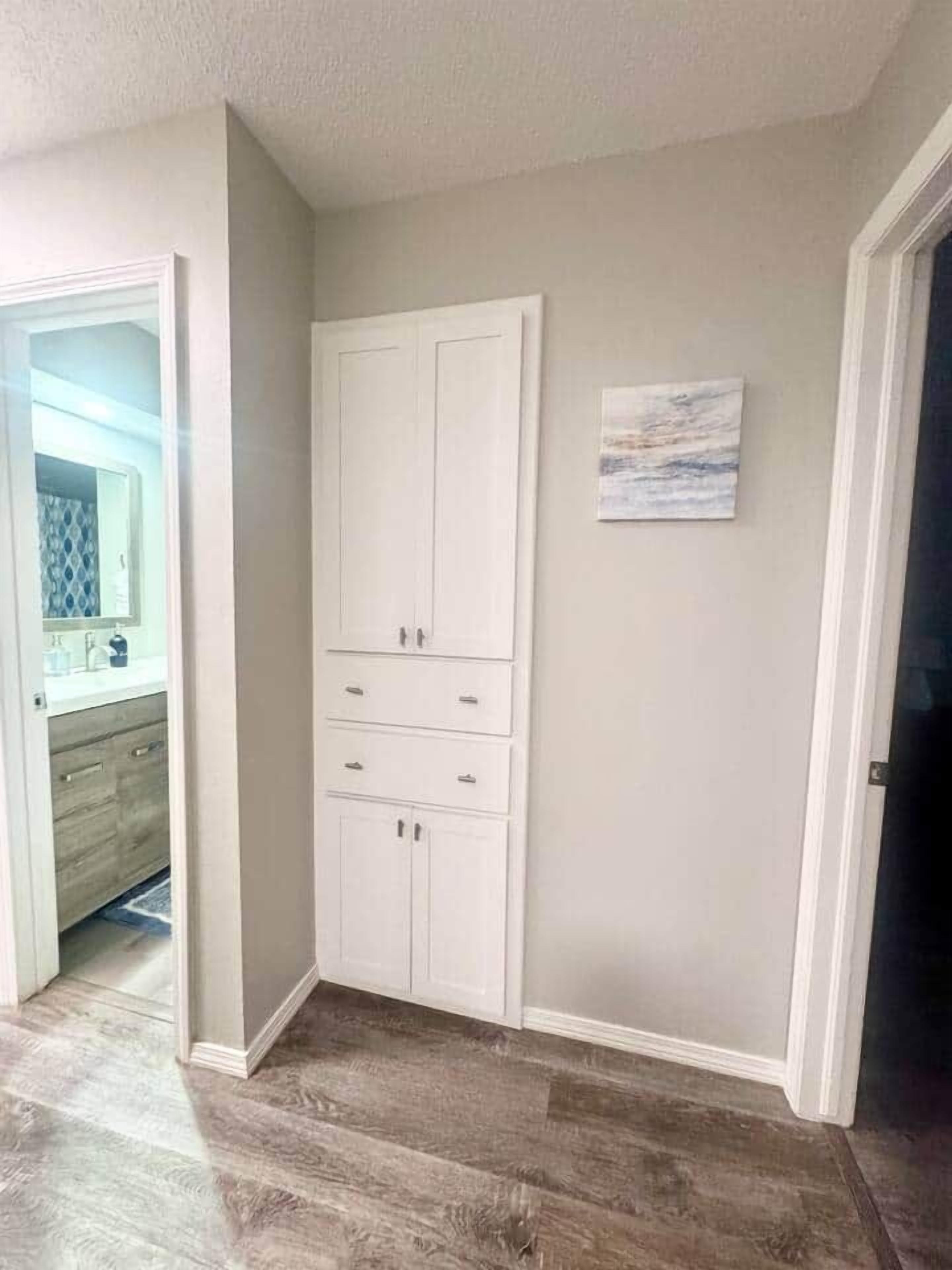 Une chambre d’angle avec une armoire blanche, un petit tableau accroché au mur et un plancher en bois.