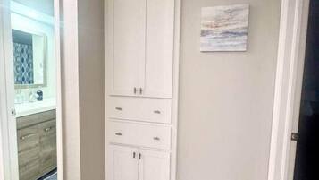 Une chambre d’angle avec une armoire blanche, un petit tableau accroché au mur et un plancher en bois.