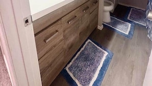 Een badkamer met een witte wastafel, een houten opbergmeubel en een spiegel.