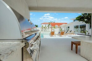 Ein Außenbereich mit Küchenzeile, Grill, Liegestühlen und Blick auf den Pool.
