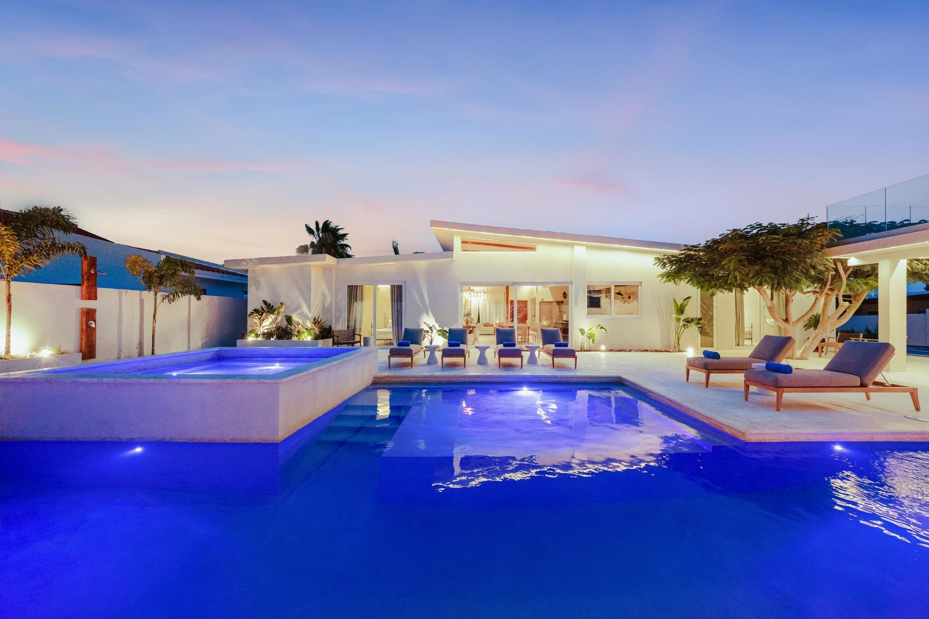 Un espace piscine extérieur moderne, doté de chaises longues et d’un intérieur bien éclairé.