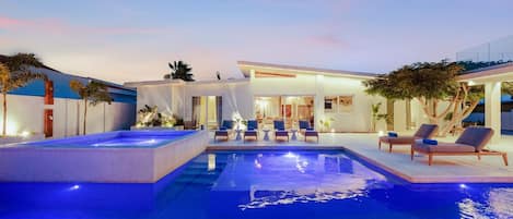 Un área de piscina moderna al aire libre con sillones de descanso e interior bien iluminado.
