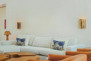 Ein Wohnzimmer mit einem hellen Sofa, zwei gemusterten Zierkissen, einem Holztisch und zwei Wandlampen.