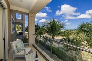 A balcony with a chair, a table, and a bottle of wine. - LeVent Sanctuary: Luxe Eagle Beach Condo 3BR 2BA (Eagle Beach)