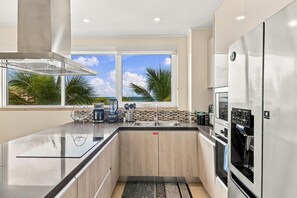 A modern kitchen with a view of the ocean, a stainless steel refrigerator, and a built-in oven. - LeVent Sanctuary: Luxe Eagle Beach Condo 3BR 2BA (Eagle Beach)