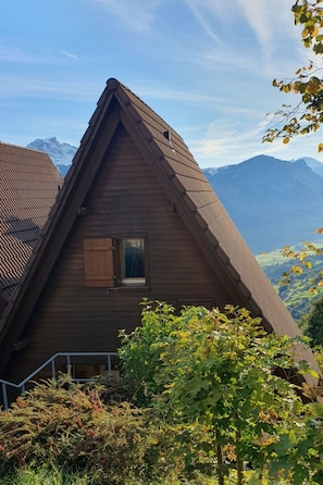 Ein hölzernes, dreieckiges Gebäude mit einem Fenster und Blick auf Berge.