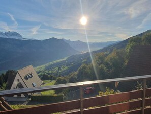 Eine Berglandschaft mit blauem Himmel, strahlender Sonne und einem Haus mit geneigtem Dach.