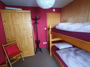 Um quarto pequeno com uma cama beliche, um guarda-roupa de madeira, uma cadeira e um cabideiro.