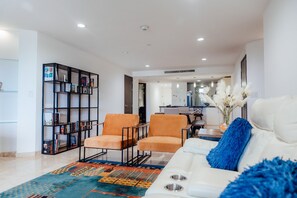 A modern living room with a sofa, two armchairs, a bookshelf, and a dining area in the background. - Luxury Oasis Retreat Near Eagle Beach 3BR 3BA (Eagle Beach)