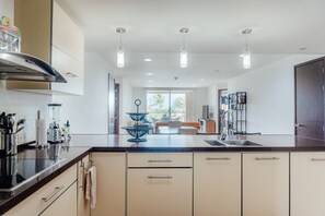 Une cuisine moderne dotée d’un îlot central, de luminaires suspendus et donnant sur un espace de vie.