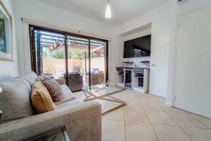 A living room with a sofa, a glass coffee table, and a sliding glass door leading to an outdoor patio. - Gold Coast Retreat: 2BR/3BA Townhome, Private Pool (Noord)