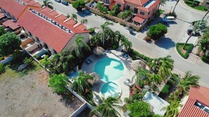 Un vecindario con piscina rodeada de palmeras y un edificio de techos rojos.