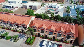 A residential area with terracotta-roofed buildings, a swimming pool, and parked cars. - Gold Coast Retreat: 2BR/3BA Townhome, Private Pool (Noord)