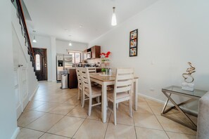 A modern kitchen with a dining area, featuring a central island, wooden chairs, and a glass table. - Gold Coast Retreat: 2BR/3BA Townhome, Private Pool (Noord)