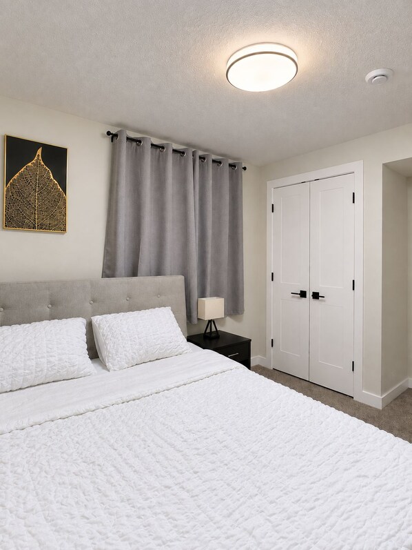 Ein Schlafzimmer mit Bett, Nachttisch, Lampe, Kleiderschrank und Deckenleuchte.