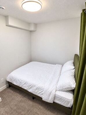 A single-bed room with a headboard, a ceiling light, and a green curtain. - Vine Luxe.

A brand-new, stylish and peaceful private 2-bedroom. (Regina)