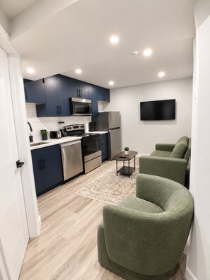 A modern kitchen with dark blue cabinets, stainless steel appliances, and a flat-screen TV mounted on the wall. - Vine Luxe.

A brand-new, stylish and peaceful private 2-bedroom. (Regina)