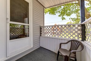 A covered porch with a chair, a window with a lattice screen, and a view of a residential area. - Beautifully Remodeled 3BR Home Near Niagara Falls! (Niagara Falls)
