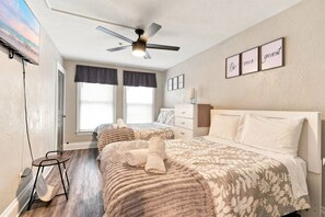 A bedroom with two beds, a ceiling fan, a TV, and a wall with framed pictures. - Beautifully Remodeled 3BR Home Near Niagara Falls! (Niagara Falls)