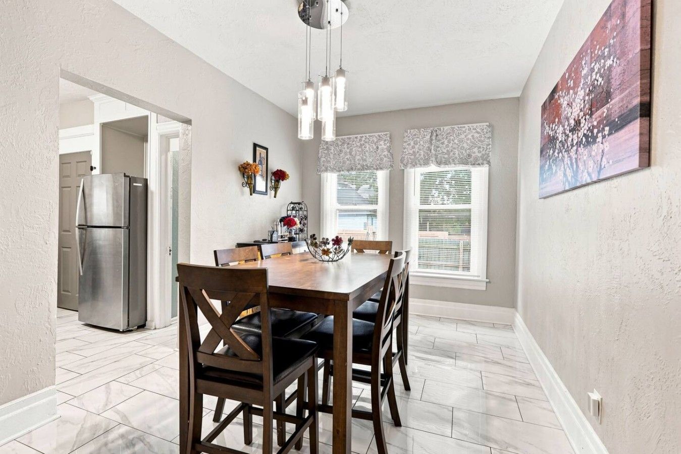 A dining area with a wooden table and chairs, a refrigerator, and a painting on the wall.