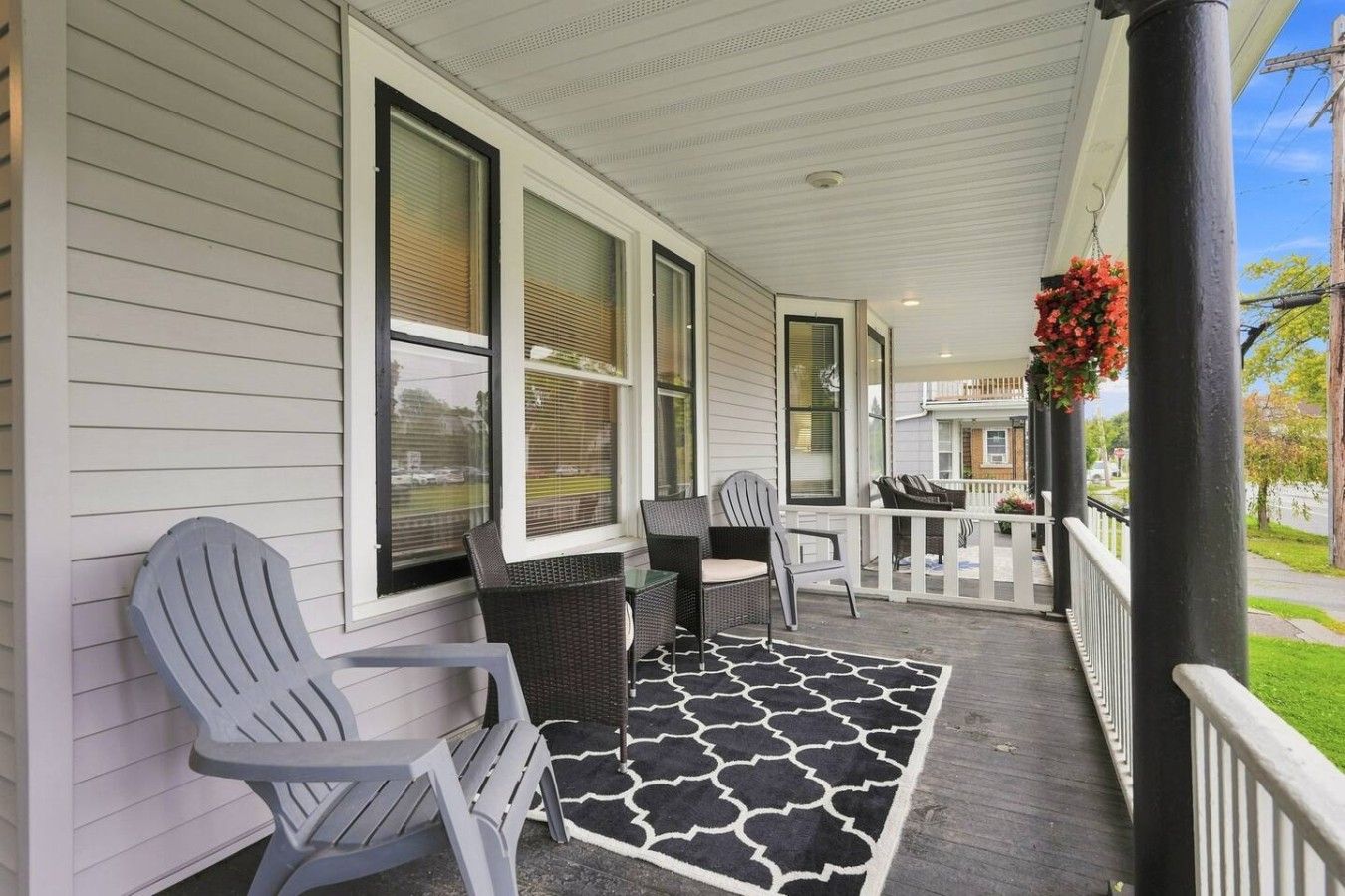 A covered porch with outdoor seating, a patterned rug, and a hanging flower arrangement.