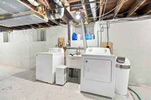 Un lavadero con dos lavadoras, un lavabo y un cubo de basura.