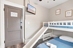 Un dormitorio con una cama litera, una puerta con un letrero, un televisor de pantalla plana y dos cuadros en la pared.