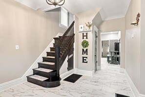 A staircase leading to a landing with a 'HOME' sign, a chandelier, and a view into a dining area. - Beautifully Remodeled 5BR Home Near Niagara Falls! (Niagara Falls)
