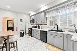 A modern kitchen with grey cabinets, a black stove, and a window with white blinds. - Beautifully Remodeled 5BR Home Near Niagara Falls! (Niagara Falls)