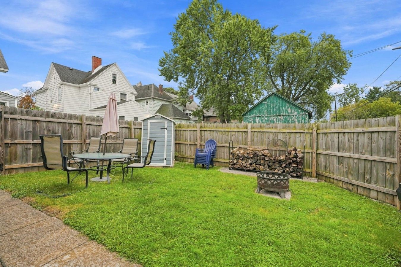 A backyard with a wooden fence, a patio table with chairs, a shed, and a green structure.