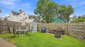 A backyard with a wooden fence, a patio table with chairs, a shed, and a green structure. - Beautifully Remodeled 4BR Home Near Niagara Falls! (Niagara Falls)