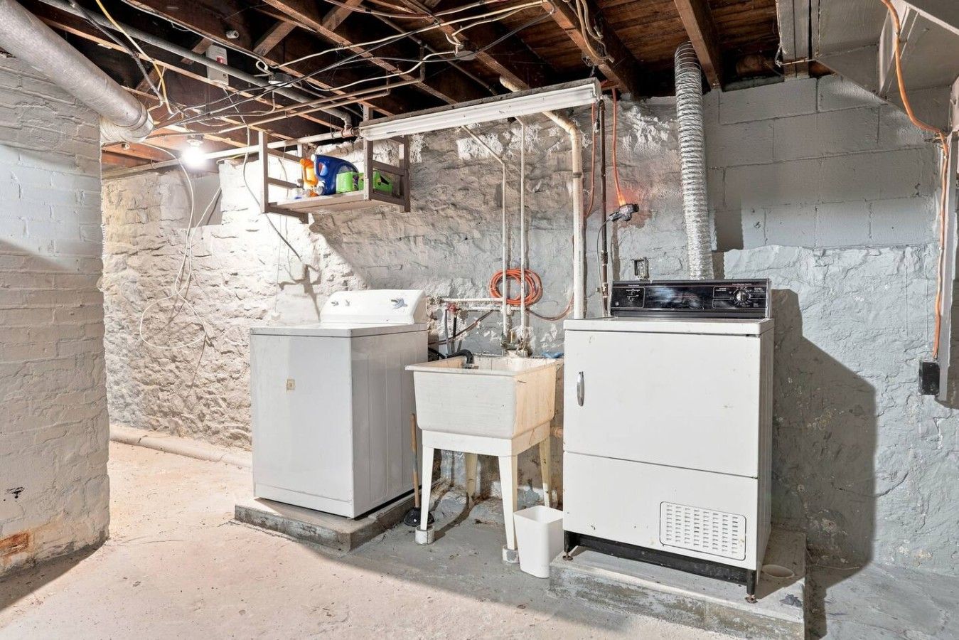 A utility room with two large white appliances, a wooden cabinet, and exposed ductwork.