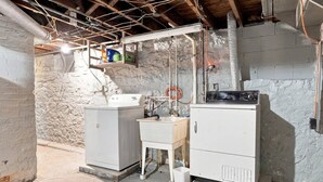 A utility room with two large white appliances, a wooden cabinet, and exposed ductwork. - Beautifully Remodeled 4BR Home Near Niagara Falls! (Niagara Falls)