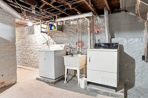 A utility room with two large white appliances, a wooden cabinet, and exposed ductwork. - Beautifully Remodeled 4BR Home Near Niagara Falls! (Niagara Falls)