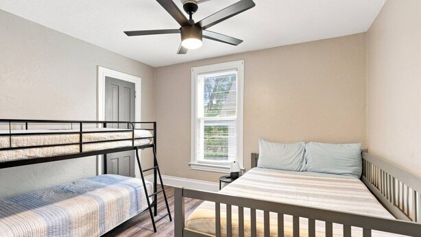 A bedroom with bunk beds, a ceiling fan, a window with blinds, and a bedside table. - Beautifully Remodeled 4BR Home Near Niagara Falls! (Niagara Falls)