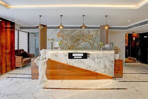 A hotel reception area with a marble counter, a reception desk, and a modern chandelier. - Palette City Formerly Emerald Guestimony (Pune)