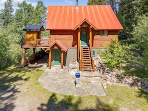 A wooden cabin with a red roof, a porch, and a stone pathway leading to the entrance. - Mountain Escape. Sauna & Soak. (Columbia-Shuswap)